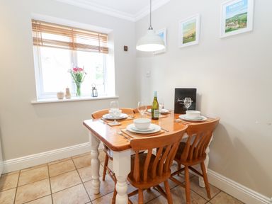 A dining area with a wooden table set for four under a hanging light at Farm View Lodge in Painswick