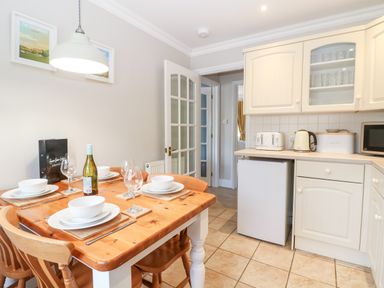 A kitchen with a wooden dining table set for four and white cabinets at Farm View Lodge in Painswick