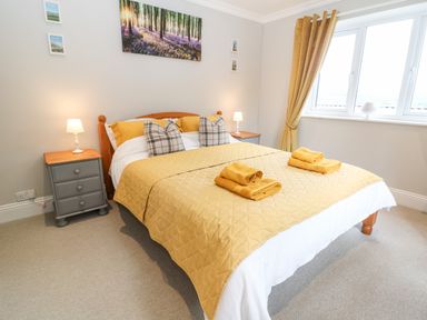 A bedroom with a double bed covered in mustard bedding and matching towels beside two bedside tables with lamps at Farm View Lodge in Painswick