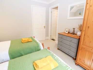 A bedroom with two single beds with green blankets and yellow towels a gray chest of drawers and a wooden wardrobe at Farm View Lodge in Painswick