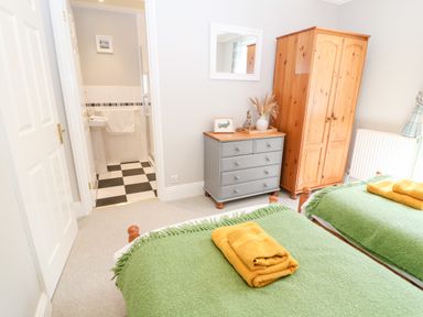 A bedroom with two beds with green covers and yellow towels two wooden wardrobes a grey chest of drawers and a bathroom with black and white checkered floor at Farm View Lodge in Painswick