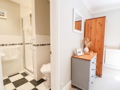 A bathroom with black and white checkered floor next to a room with gray chest of drawers and wooden wardrobe at Farm View Lodge in Painswick
