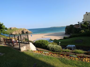 A beach with sand and people in the distance with a grassy area and flower bed in the foreground by Westwinds in Tenby