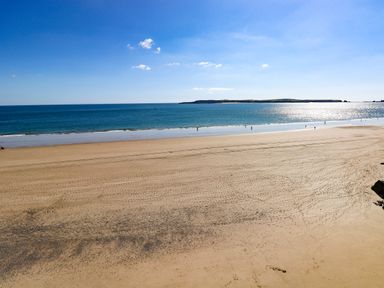 A sandy beach with footprints and calm sea water under a clear blue sky at Westwinds in Tenby