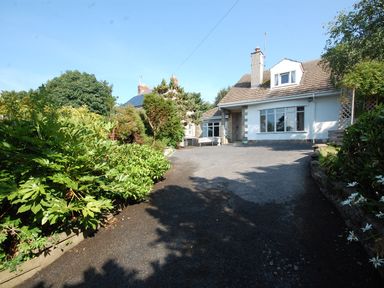 A driveway with plants and trees leading to a white house with a chimney at Westwinds in Tenby