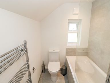 A bathroom with a toilet a bathtub a chrome towel radiator and a small window at Westwinds in Tenby