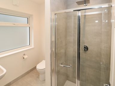 A bathroom with a shower enclosure a toilet a small sink and a frosted window at Westwinds in Tenby