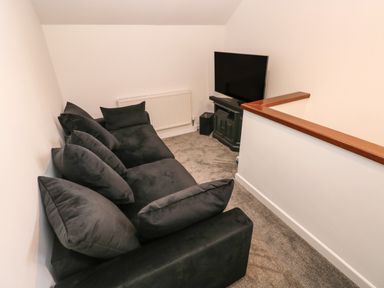 A small room with a black sofa facing a television on a stand at Westwinds in Tenby