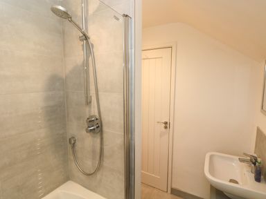 A bathroom with a shower area and a sink near a closed door at Westwinds in Tenby