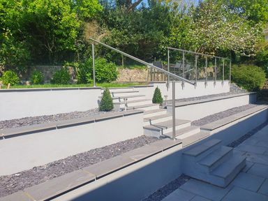 A tiered garden with stairs metal handrails and a seating area with glass fencing at Westwinds in Tenby