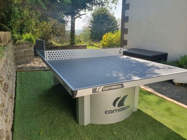 An outdoor table tennis table on a patch of artificial grass next to a stone wall and a white building at Westwinds in Tenby