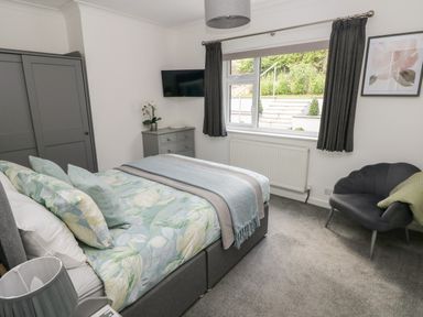 A bedroom with a bed a wardrobe a chest of drawers a window and a chair at Westwinds in Tenby