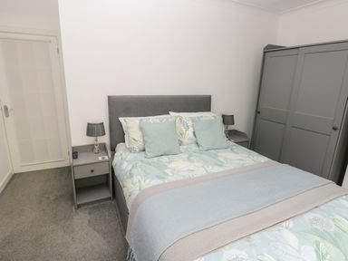 A bedroom with a bed with patterned bedding two pillows two bedside tables with lamps and a wardrobe at Westwinds in Tenby