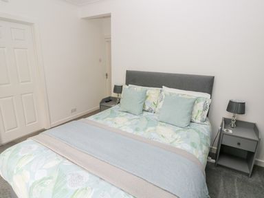 A bedroom with a double bed with leaf patterned bedding and two bedside tables at Westwinds in Tenby