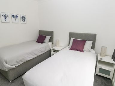 A bedroom with two single beds two pillows on each bed bedside tables with lamps and animal prints on the wall at Westwinds in Tenby