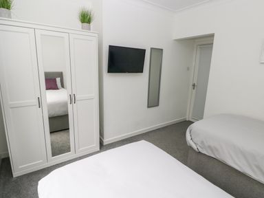 A bedroom with a white wardrobe with mirrored door two beds a wall mounted television and a door at Westwinds in Tenby