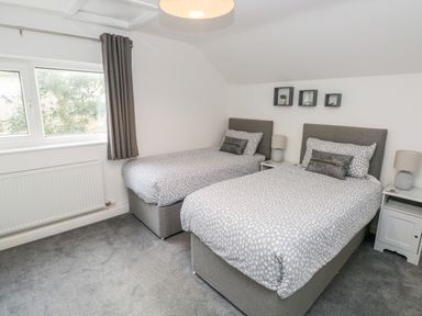 A bedroom with two single beds bedside tables lamps and a window at Westwinds in Tenby