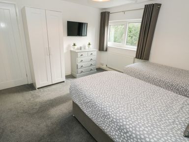 A bedroom with two single beds a white wardrobe a gray chest of drawers with plants and a wall-mounted tv at Westwinds in Tenby