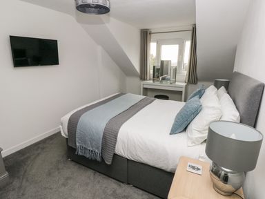 A bedroom with a bed a grey lamp a wall mounted tv and a dressing table with mirror at Westwinds in Tenby