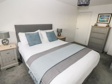 A bedroom with a double bed two bedside tables with lamps a chest of drawers and a door at Westwinds in Tenby