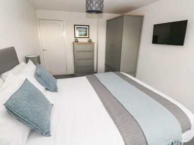 A bedroom with a bed pillows a chest of drawers a wardrobe and a wall mounted television at Westwinds in Tenby