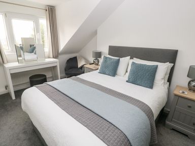 A bedroom with a bed with pillows and blankets a dressing table a chair and bedside tables at Westwinds in Tenby