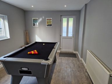 A game room with a pool table with balls set up a door and two framed pictures on the wall at Westwinds in Tenby