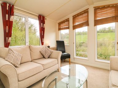 A living room with beige sofas a glass coffee table and a black chair near windows with wooden blinds at Exe Valley Lodge in Bampton Devon