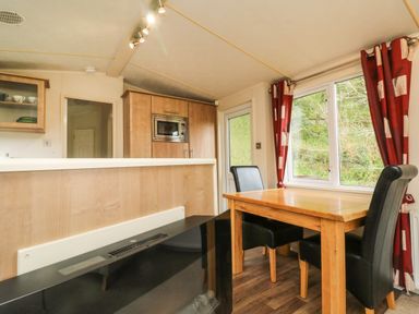 A dining area with a wooden table and black chairs next to a window with red curtains in a kitchen space at Exe Valley Lodge in Bampton Devon