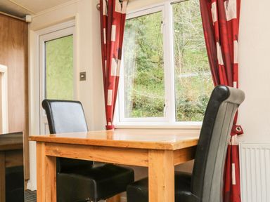A wooden dining table with two black leather chairs near a window with red curtains at Exe Valley Lodge in Bampton Devon