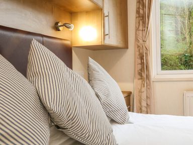 A bedroom with striped pillows on a bed near a window and wooden cabinets at Exe Valley Lodge in Bampton Devon