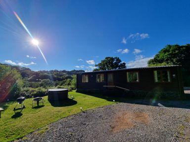 A cabin with lawn chairs and a hot tub under a sunny sky at Exe Valley Lodge in Bampton Devon