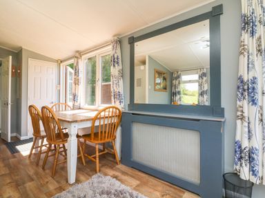 A dining area with a wooden table and four chairs near windows with floral curtains at Valley Lodge in Bampton Devon