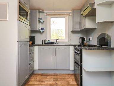 A kitchen with grey cabinets a black oven a window above the sink and wooden flooring at Valley Lodge in Bampton Devon
