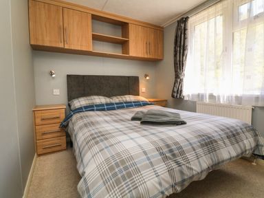 A bedroom with a double bed with plaid bedding two wooden bedside tables and wooden cabinets above at Valley Lodge in Bampton Devon
