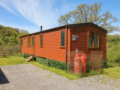An orange mobile home with windows a door and gas tanks outside surrounded by grass and trees at Valley Lodge in Bampton Devon