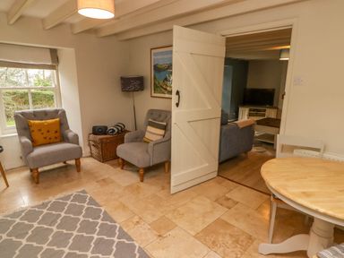 A seating area with two armchairs and a wicker basket beside a doorway leading to a room with a sofa and TV at Sea View Newport Pembrokeshire