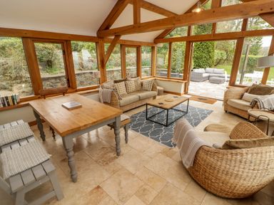 A sunroom with wooden beams glass windows and doors wicker armchairs a wooden table with benches and sofas at Sea View in Newport Pembrokeshire