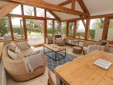 A sunroom with wicker furniture and a wooden table overlooking a garden at Sea View in Newport Pembrokeshire