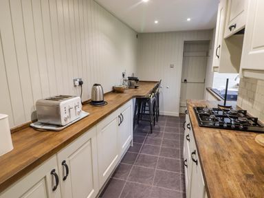 A kitchen with wooden countertops white cabinets a gas stove toaster kettle and bar stools at Sea View in Newport Pembrokeshire