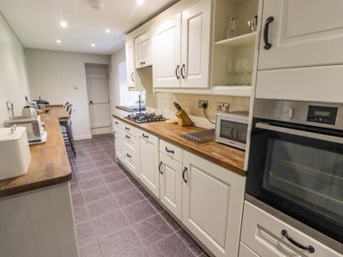 A galley kitchen with wooden countertops white cabinets and appliances at Sea View in Newport Pembrokeshire