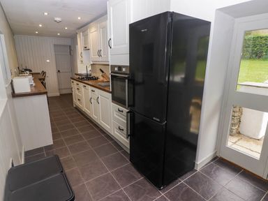 A kitchen with white cabinets a black refrigerator a built in oven and a door leading outside at Sea View in Newport Pembrokeshire