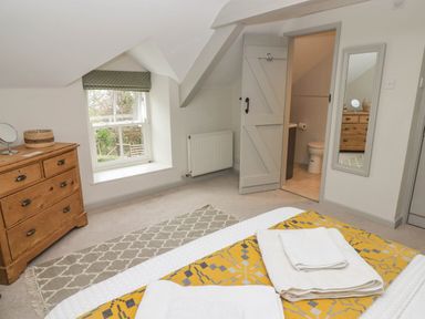 A bedroom with a wooden dresser a window with a green blind a bed with folded towels and an open door showing a bathroom at Sea View in Newport Pembrokeshire