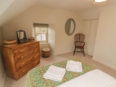 A bedroom with a wooden chest of drawers a chair a round wall mirror and folded towels on a bed at Sea View in Newport Pembrokeshire