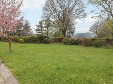 A garden with grass lawn flowering trees and shrubs with hills in the background at Sea View in Newport Pembrokeshire