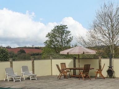 An outdoor patio area with loungers and a table with chairs under an umbrella at The Pool House in Crediton