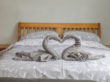A bed with a wooden headboard and two towel swans on the bedding at The Pool House in Crediton