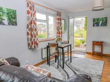 A small dining table with two chairs near a window and open door in a living room at The Pool House in Crediton