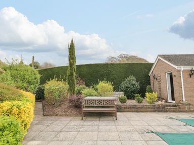 A patio with a bench and various shrubs next to a brick building at The Pool House in Crediton