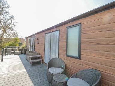 An outdoor deck with wicker chairs and a wooden wall at Dreams & Streams in Bockenfield Country Park near West Thirston